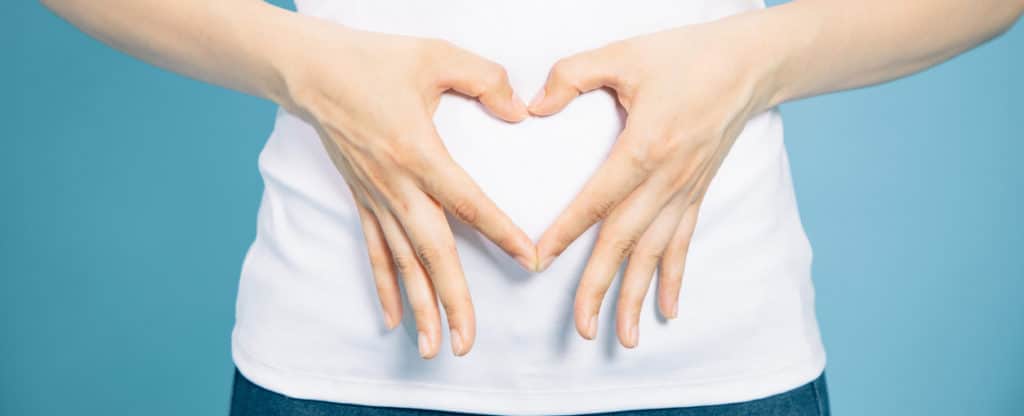 young woman who makes a heart shape by hands on her stomach.