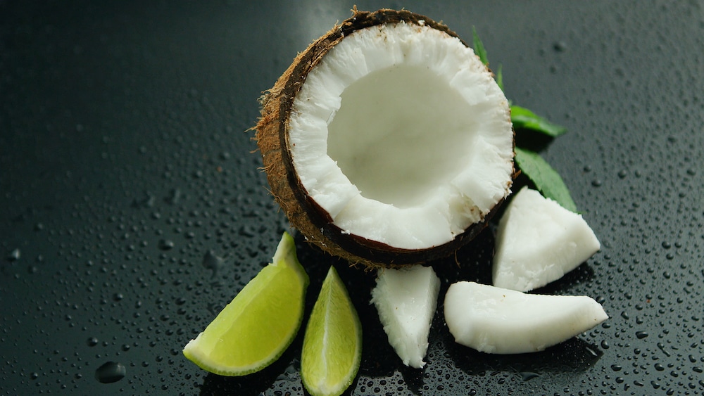 White half of fresh delicious coconut and slices of lime composed on wet glass surface