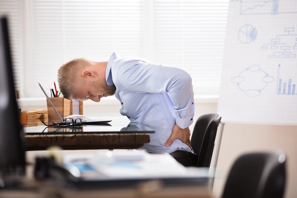 Businessman Sitting At Desk With Laptop Having Back Pain In Office